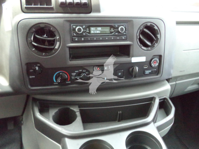 Ford E350 dash area showing factory radio, two circular air vents, climate controls, and lower storage compartments.
