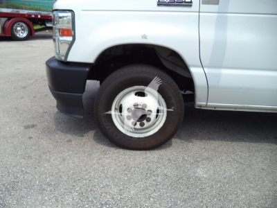 Front passenger-side wheel and fender of a white 2022 Ford E350 high cube cutaway van, showing wheel, tire, and a badge on the door; partial front bumper visible.