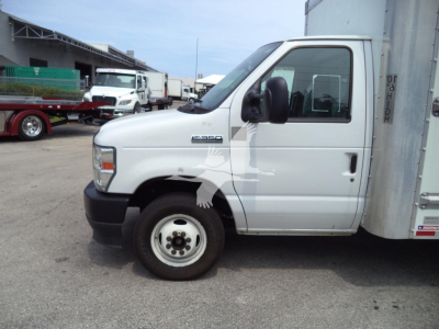 Side view of a white Ford E-350 cutaway/box truck showing front wheel, cab, and cargo box with some text on the door window.