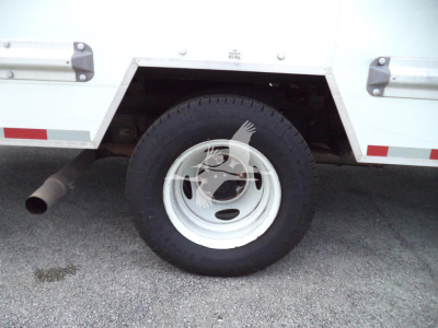 Truck wheel and rear side of a 2022 Ford E350 cargo box with white painted wheel, side step and exhaust visible.