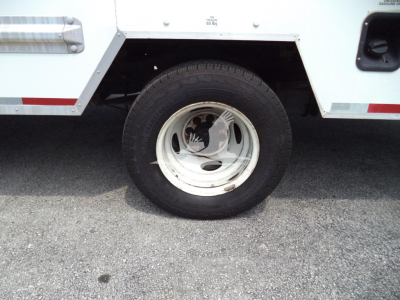 Wheel and tire on Ford E350 utility truck with white steel rim, underbody panel, and side step visible.