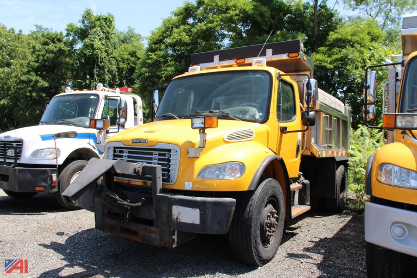 Dump truck front view showing yellow Freightliner M2 106 dump body and protective bumper.
