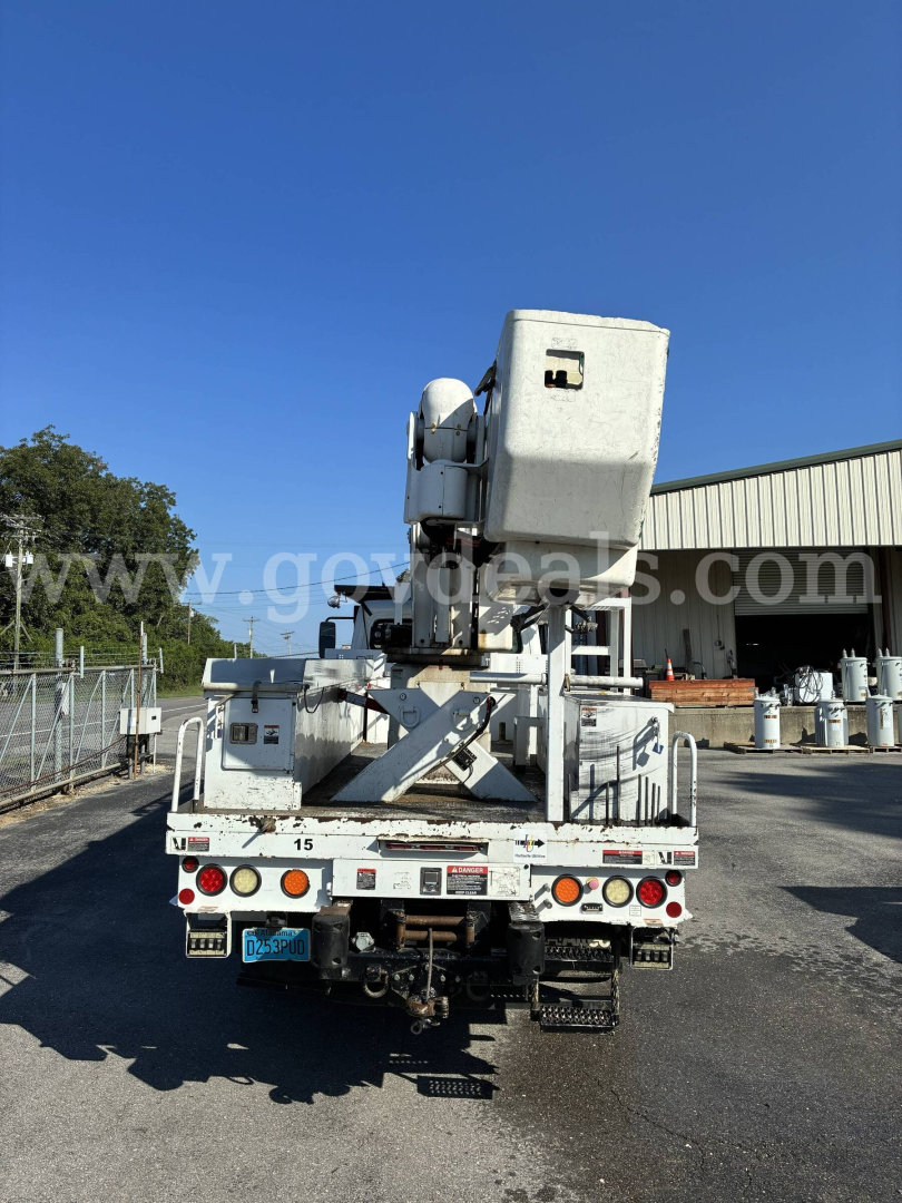 Truck bed of a Freightliner M2 106 bucket truck with elevated bucket in raised position, rear view showing platform, hydraulic outriggers, and spare wheels.