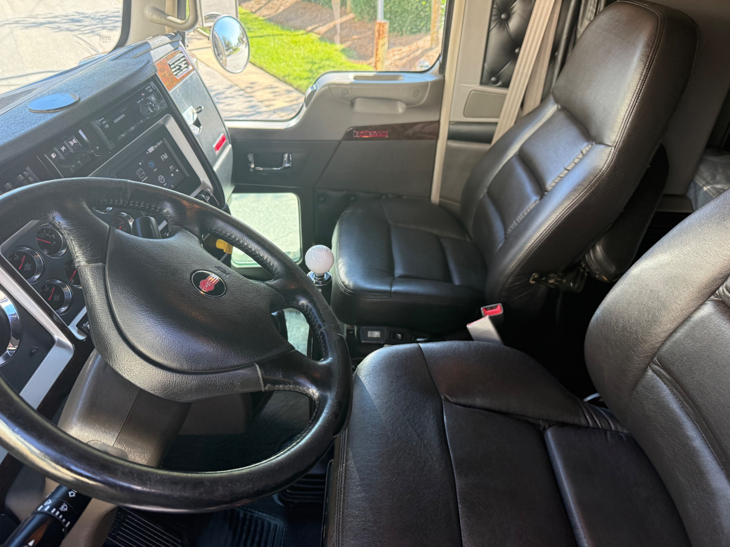 Kenworth W900L truck cabin interior showing steering wheel and driver's seat with black leather upholstery; dashboard and door panels visible.
