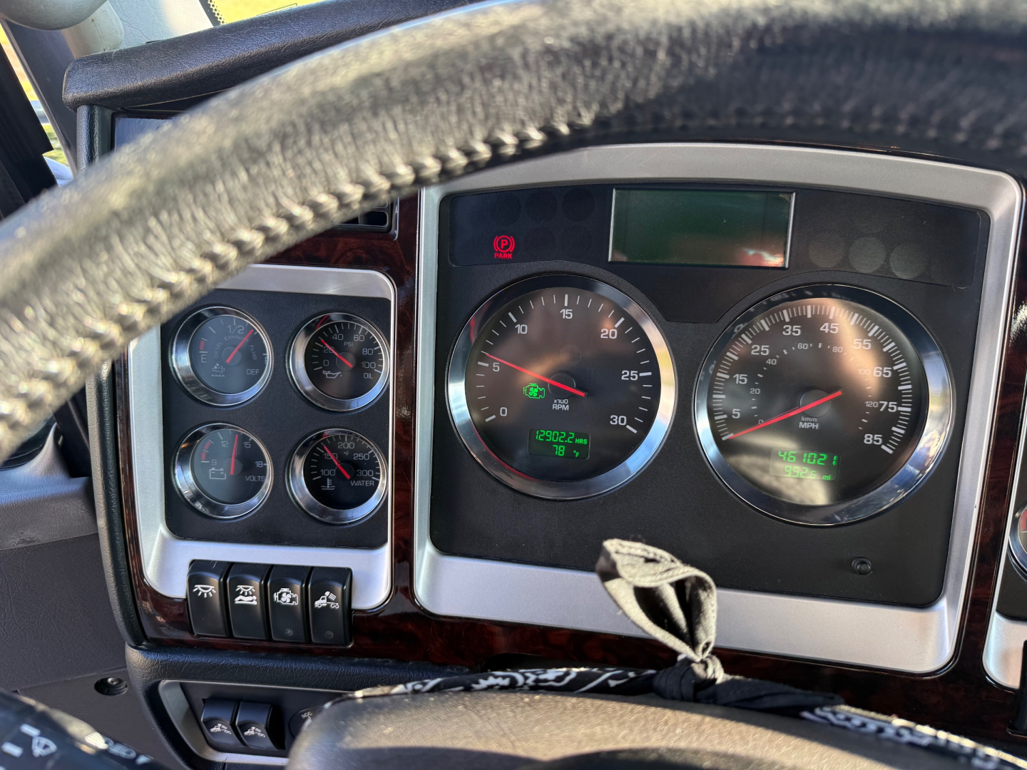 Dashboard of a Kenworth truck showing multiple analog gauges and steering wheel; central speedometer and tachometer; some warning lights; wood trim around gauges.
