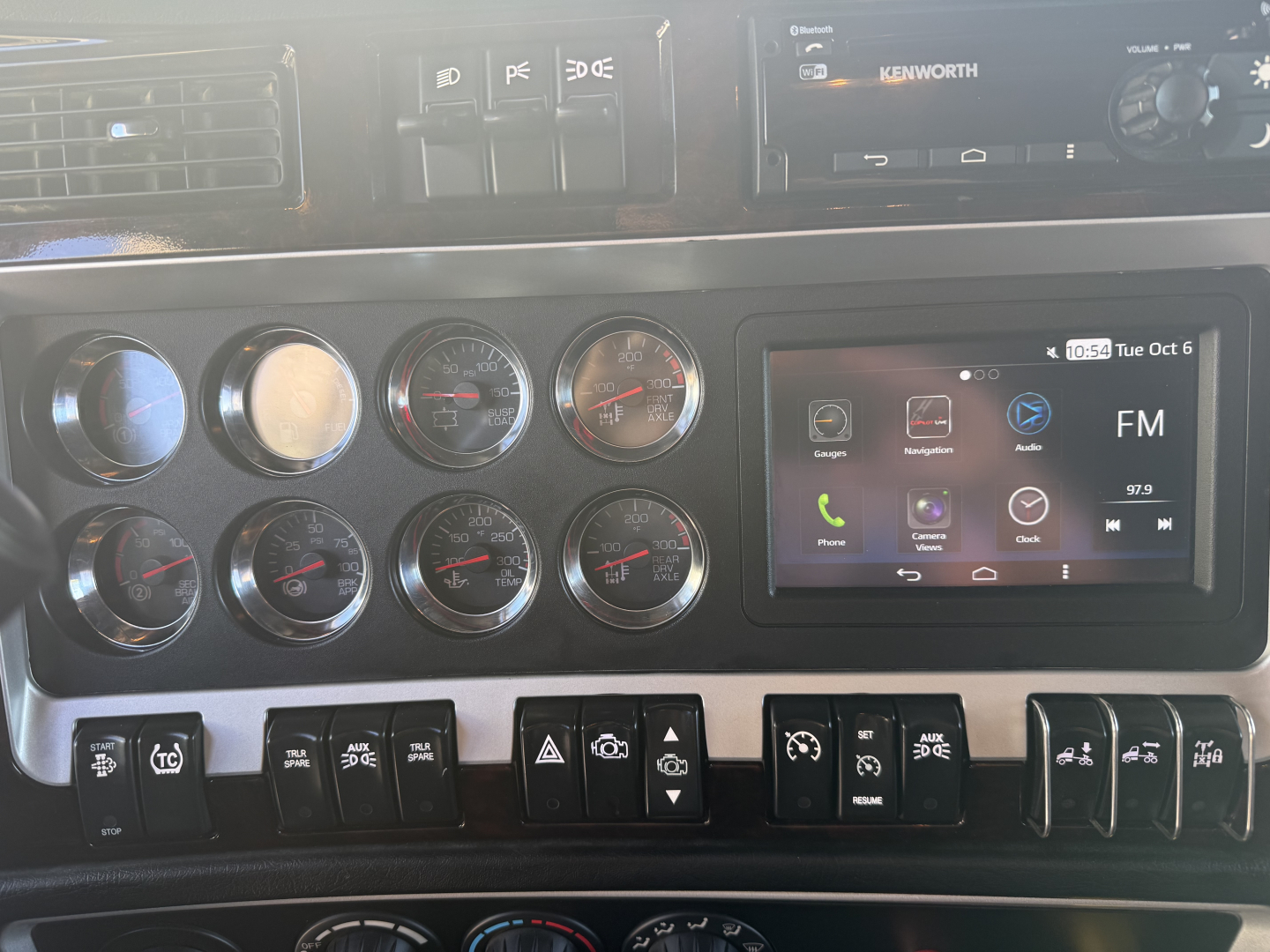 Kenworth W900L cab interior dashboard gauges and infotainment display showing multiple round gauges and a touchscreen radio.
