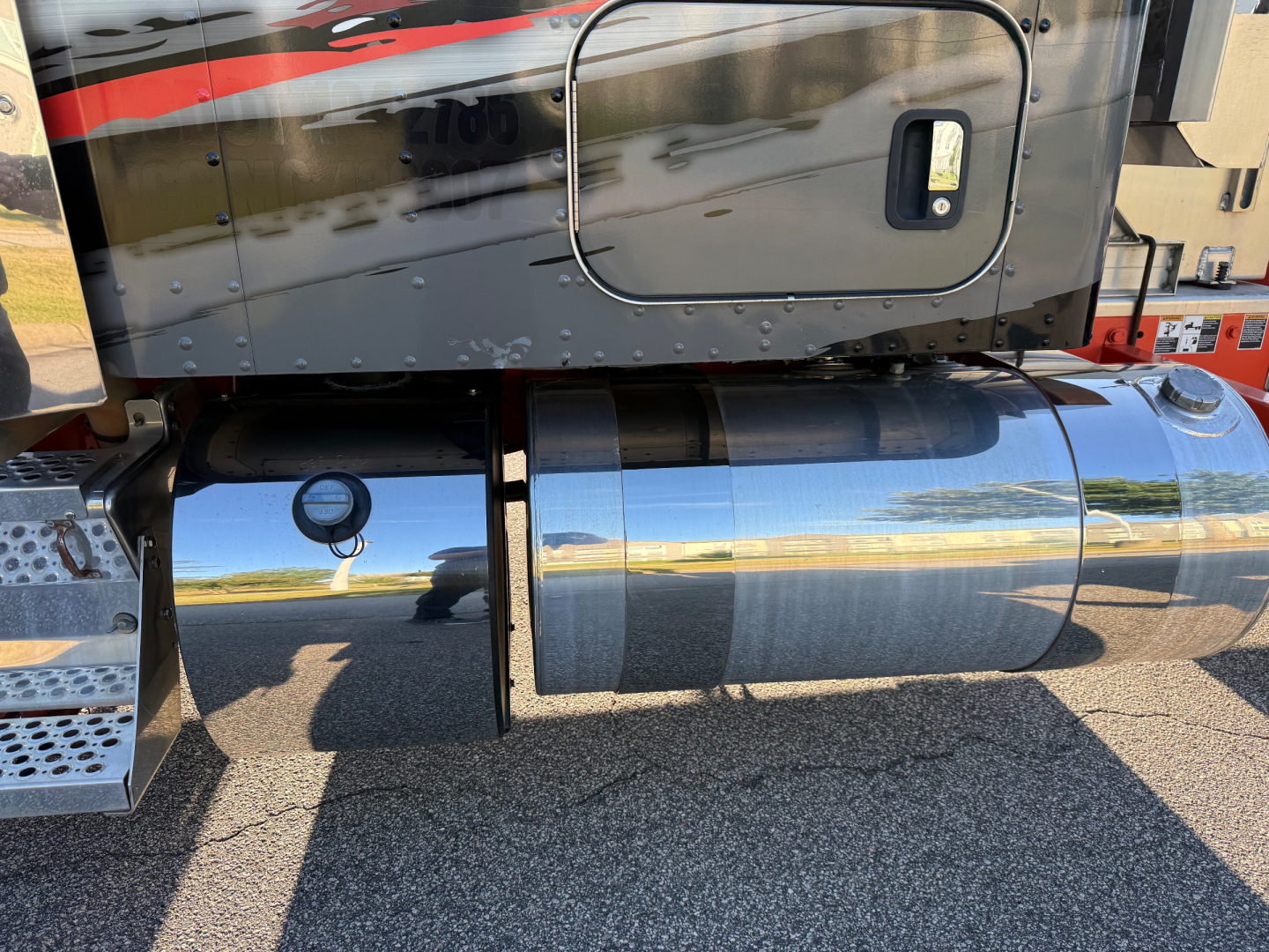 Kenworth W900L fuel tank area and lower side of cab showing chrome cylindrical fuel tank and side steps.