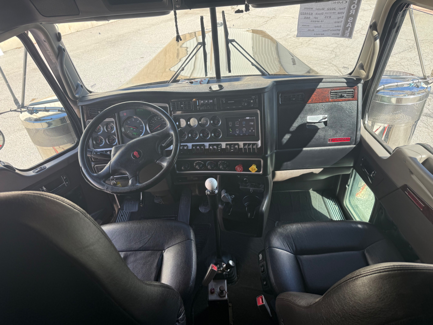Kenworth W900L cab interior showing dashboard with gauges, steering wheel, gear shifter, and center console; various control panels and cup holders visible.