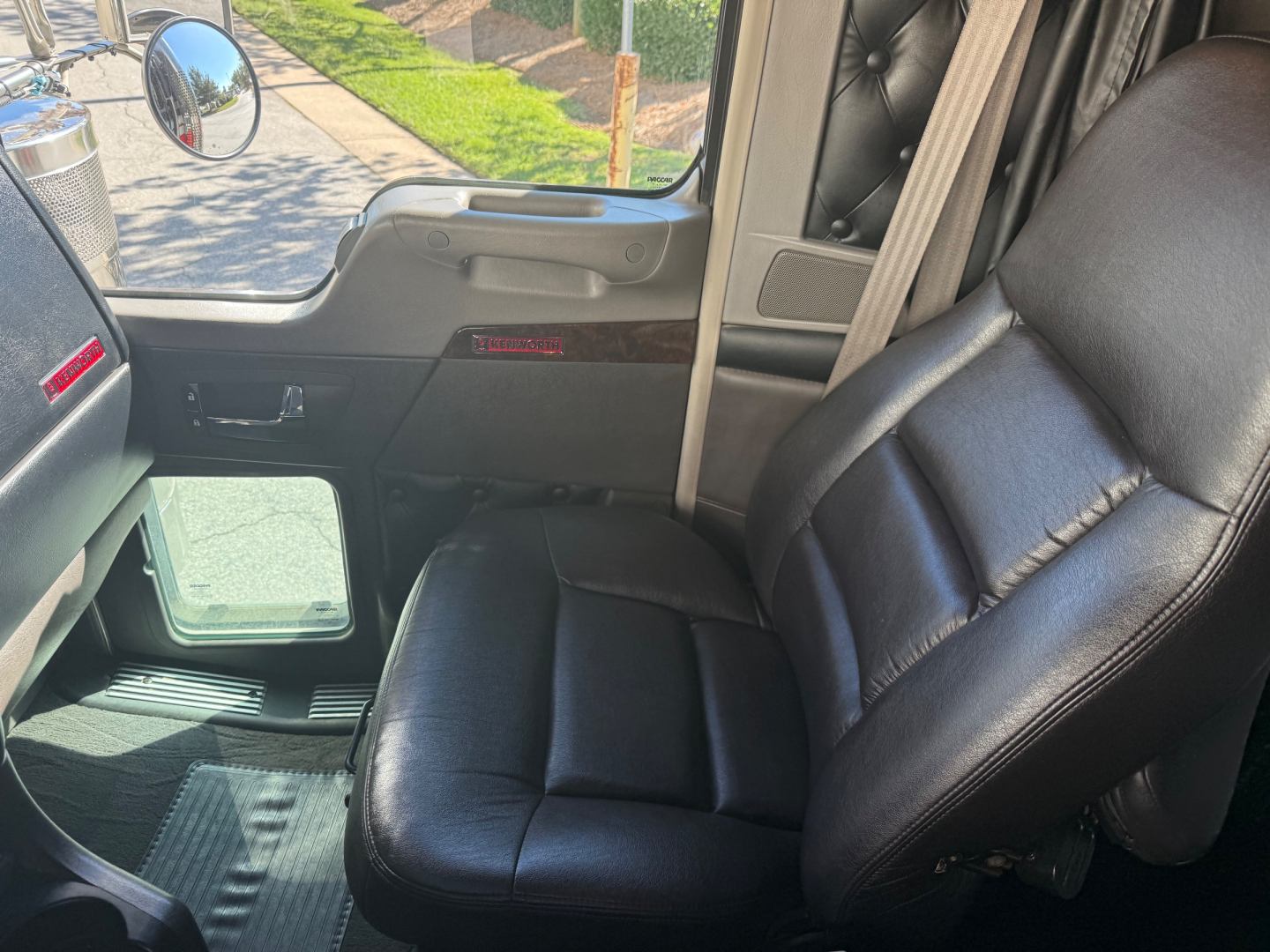Kenworth W900L interior seat and door panel view with black leather seat, window, and dashboard accents.