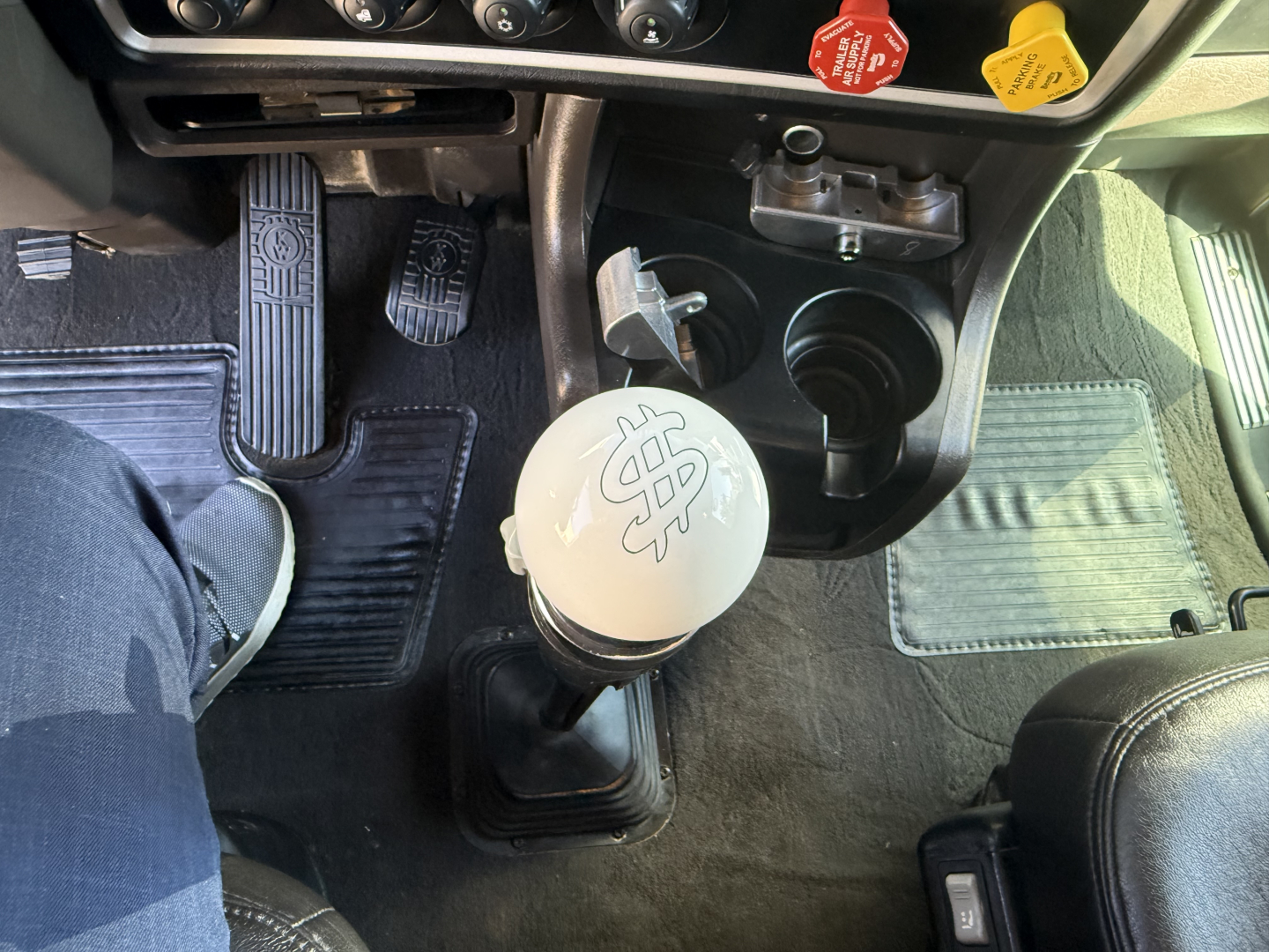 Kenworth W900L interior gear stick and dashboard view with shifter knob and pedal area.