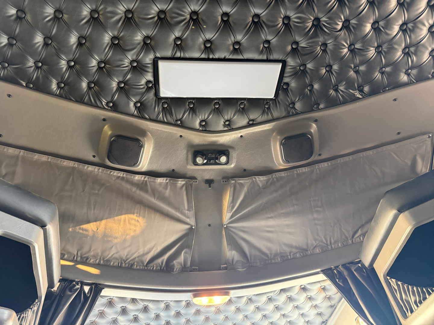 Cab interior of a Kenworth W900L showing quilted headliner, sunroof hatch, and sleeper cab storage panels.