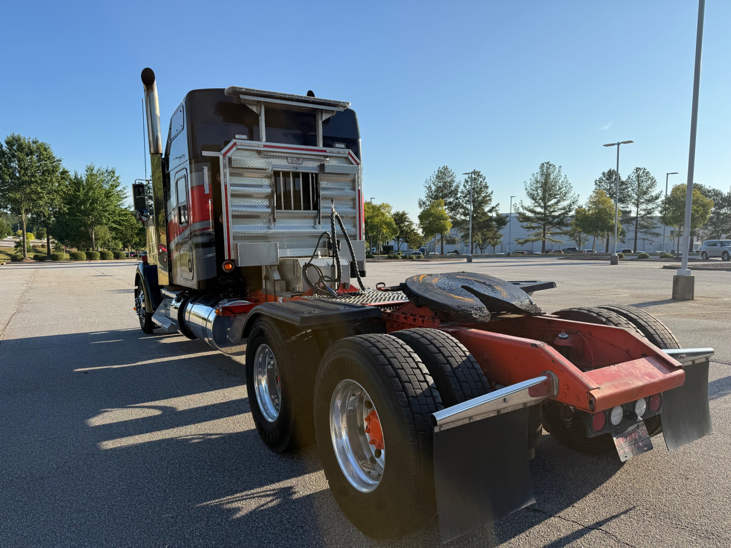 Kenworth W900L tractor rear view showing fifth wheel and dual rear tires with chrome exhaust stacks and metal toolbox; no visible text.