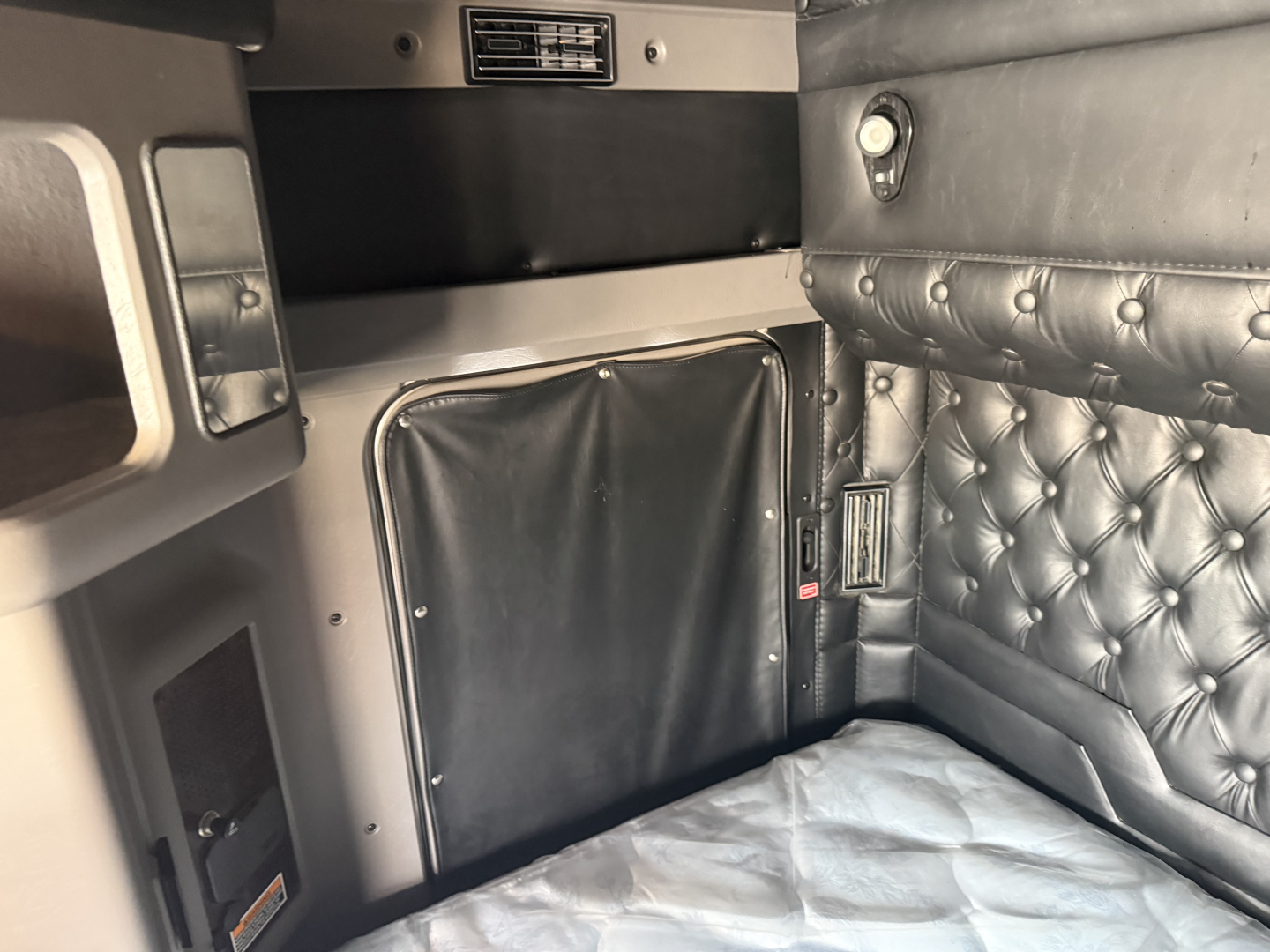 Kenworth W900L sleeper cab interior with tufted leather bed area and storage cabinet.