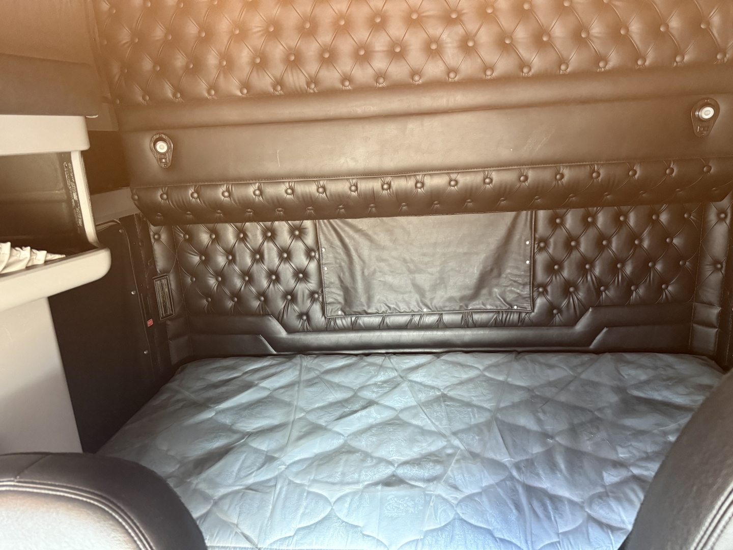 Kenworth W900L sleeper cab interior with tufted black leather seating and quilted bed cover.