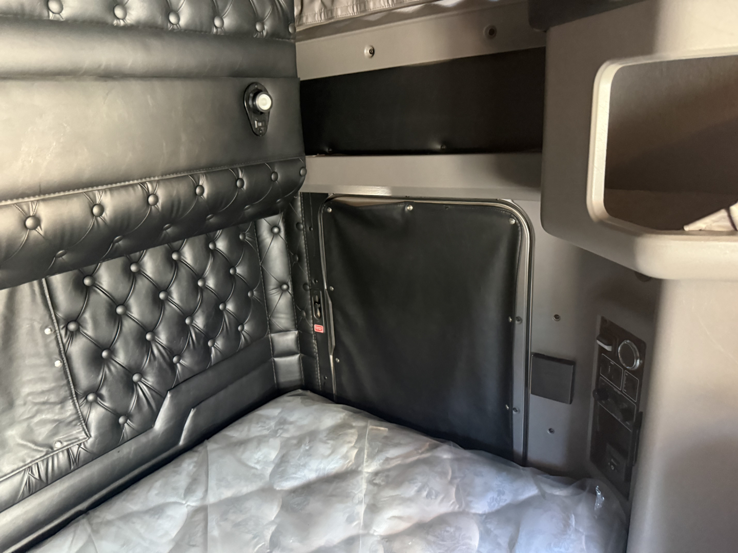 Kenworth W900L sleeper cab interior showing quilted black leather bunk area and side panel with controls.