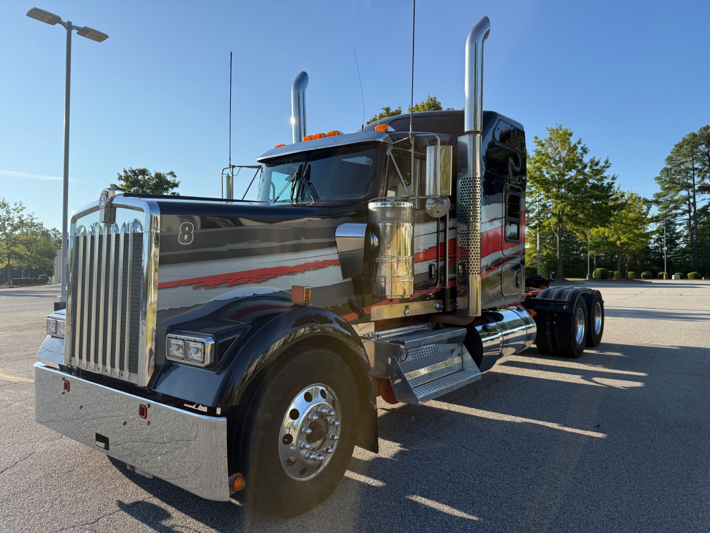 Kenworth W900L conventional sleeper truck showing chrome grille, dual exhaust stacks, polished aluminum fuel tanks, and large front bumper.