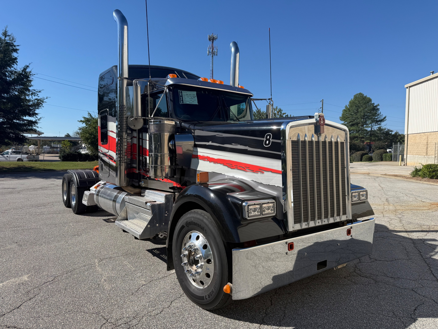 Kenworth W900L tractor in black with chrome exhaust stacks and grille, chrome bumper, fuel tanks, and red/gray graphics. Includes vertical exhaust stacks, dual rear axles, front grille and headlights visible.