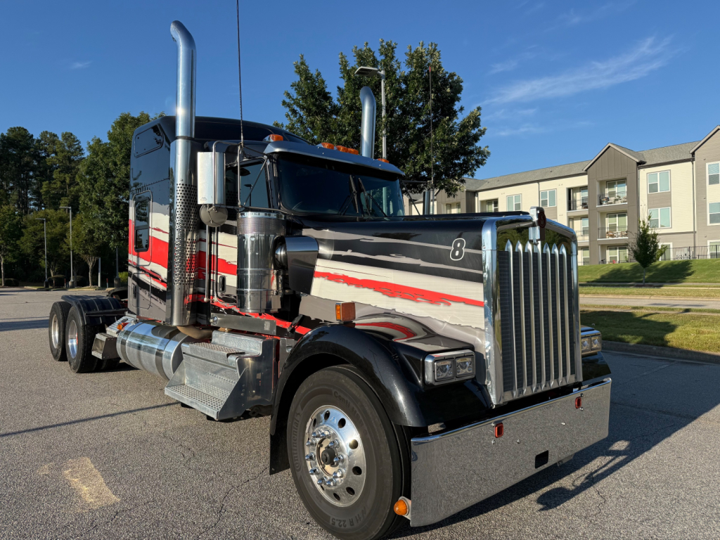 Kenworth W900L truck in black with chrome grille, large vertical exhaust stacks, and red-white stripes on the cab, front view with sleeper, chrome fuel tanks, and dual rear axles.