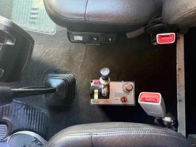 Kenworth W900L cab interior showing gear shift, control panel, and serial/DMV gauges with red seatbelt buckles.