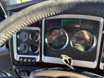 Dashboard of a Kenworth truck showing multiple analog gauges and steering wheel; central speedometer and tachometer; some warning lights; wood trim around gauges.