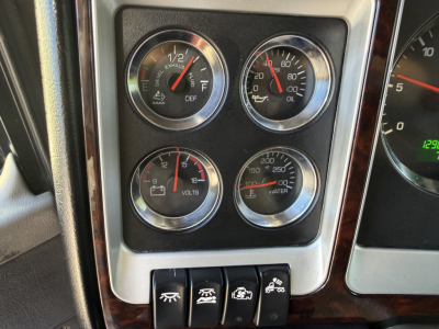 Kenworth W900L interior dashboard showing four gauges (E-DEF, volts, water temp) and switches located below, with steering column edge visible.