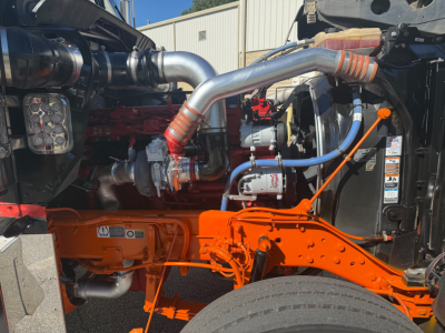 Kenworth W900L engine bay showing large intake piping and orange-painted chassis with visible turbo and hoses.