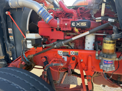 Kenworth W900L engine bay showing Cummins ISX5 engine with orange/red paint, coolant reservoir, filter canister, hoses, and wiring.