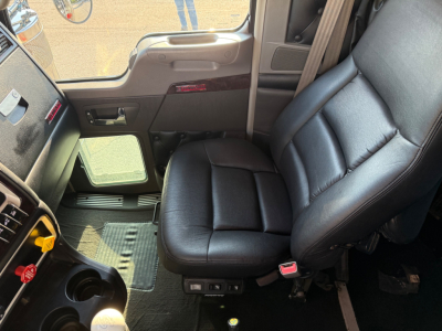 Kenworth W900L truck interior showing driver's seat and part of dashboard with control panel and door. Leather seat and steering area visible.