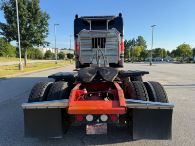 Kenworth W900L tractor rear view showing fifth wheel, dual rear axles, mud flaps, tail lights, and rear bumper with dealer plate. VIN/stock not visible on image.