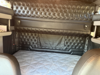Kenworth W900L cab interior with tufted black leatherette walls and quilted floor; sleeper area with elevated side shelves and a padded back panel.