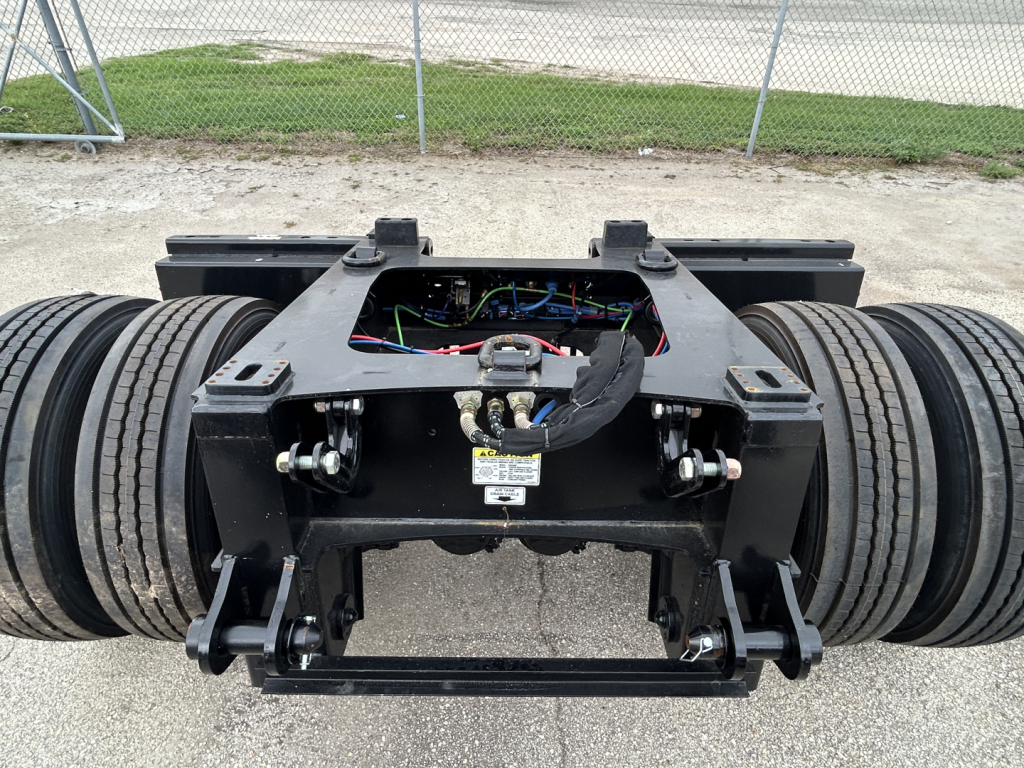 Load King trailer flip axle chassis showing wiring and connectors, dual axles with large tires, black steel frame, exposed mechanical components.