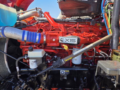 Kenworth T680 engine bay with bright red engine and label MEX15? on valve cover; visible blue hose, white reservoir, and various cables in view.