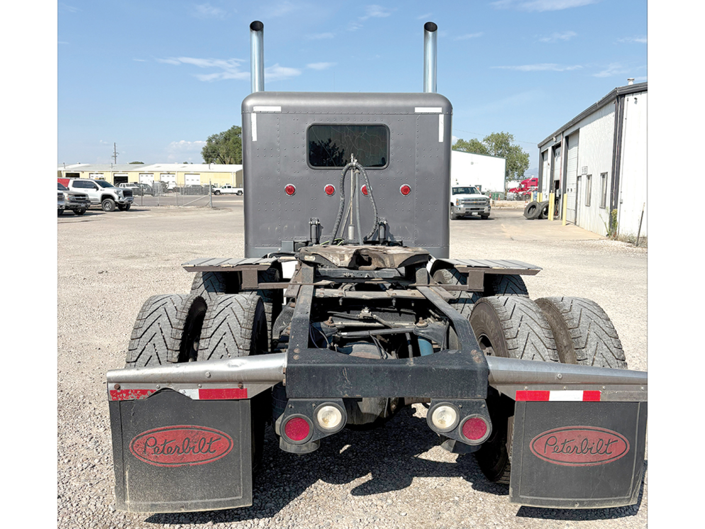Peterbilt truck chassis rear view with dual rear axles and mud flaps showing Peterbilt logos.