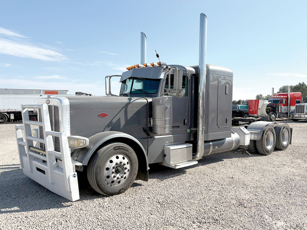 Peterbilt 389 Extended Hood conventional sleeper truck in gray, with tall exhaust stacks and front bumper guard, side view showing 6x4 tractor with dual rear axles.