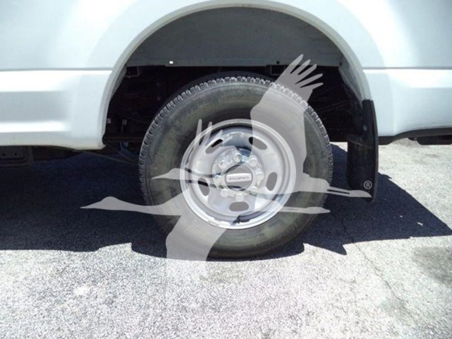 Ford F-250 wheel and front fender showing steel rim and tire, partial body in light silver, wheel well and suspension components visible.