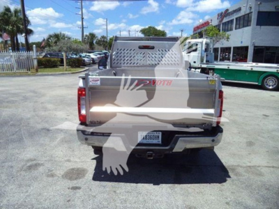 Ford F-250 dump truck rear view showing metal cargo bed and bumper with license plate, dealership lot in background.