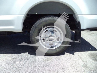 Ford F-250 wheel and front fender showing steel rim and tire, partial body in light silver, wheel well and suspension components visible.