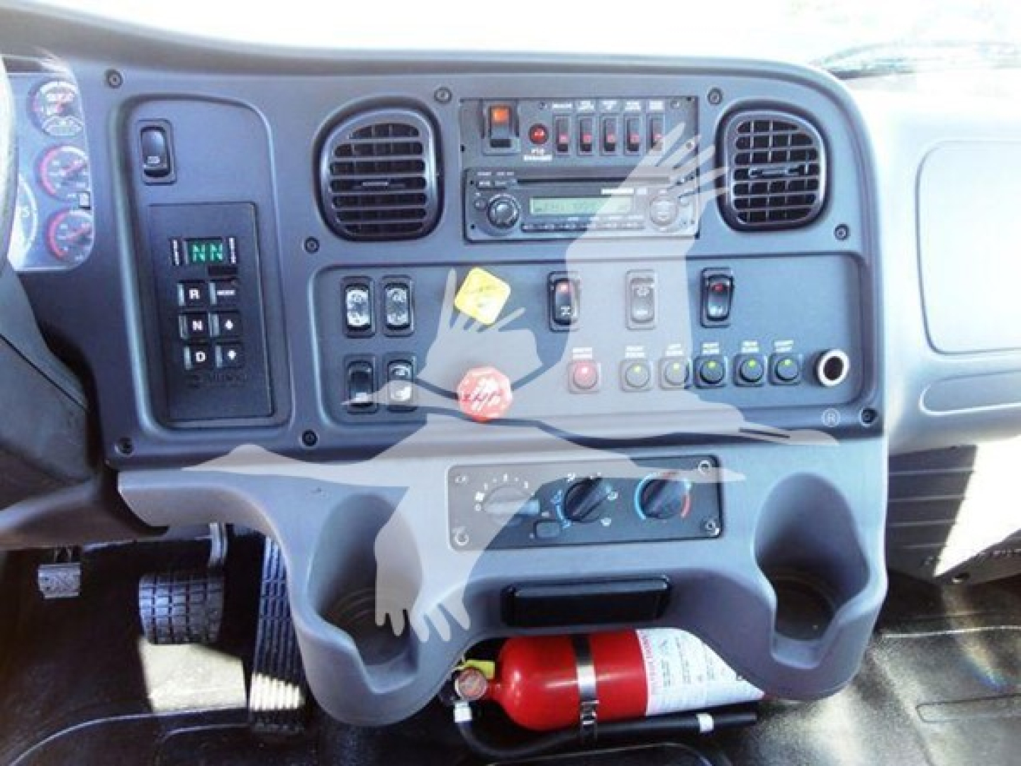 Dashboard view of a Freightliner Business Class M2 106 cabin showing instrument panel, switches, and a mounted fire extinguisher.