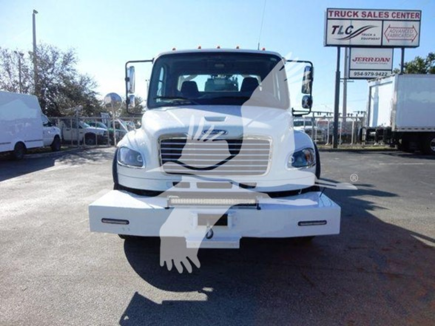 Front view of a white Freightliner бизнес class M2 106 truck with a winch category; visible dealership signs in background.