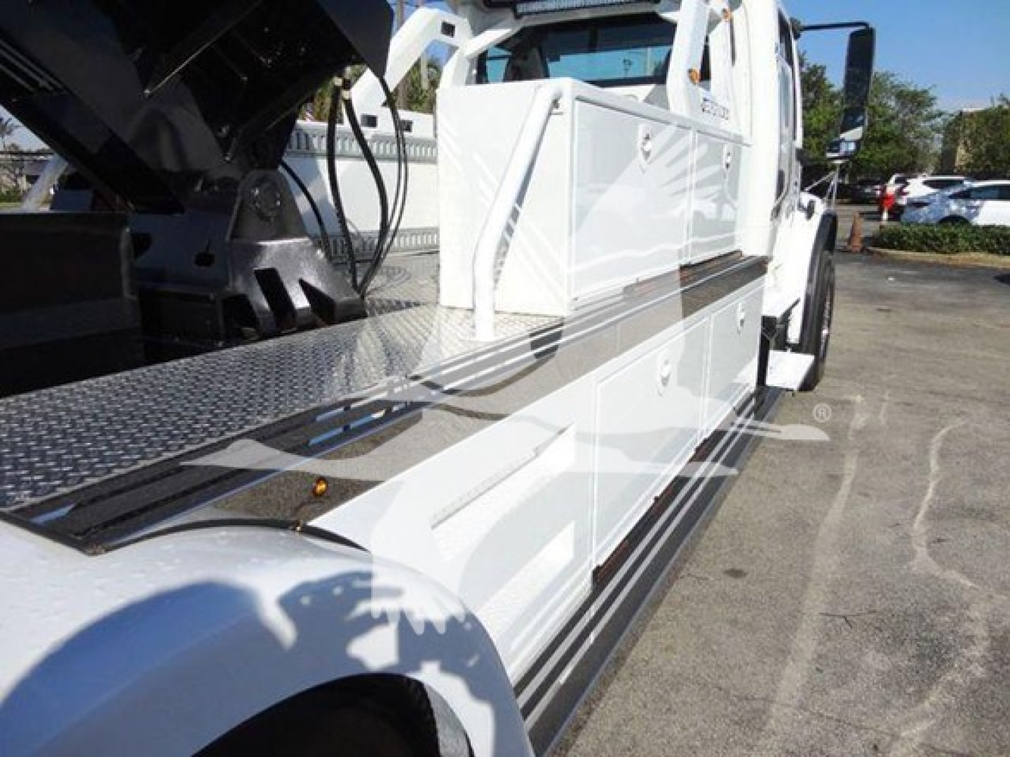 Tow truck with white body and black winch setup; long side step with diamond plate, cab in view.