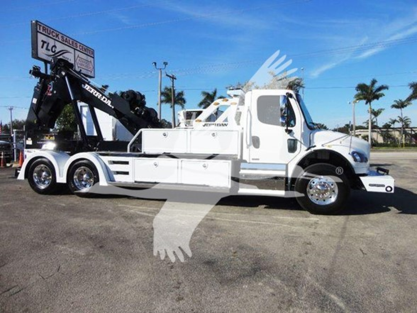 Side view of a white Freightliner Business Class M2 106 tow/winch truck with a black crane arm, chrome wheels, and lettering, shown on a dealership lot.