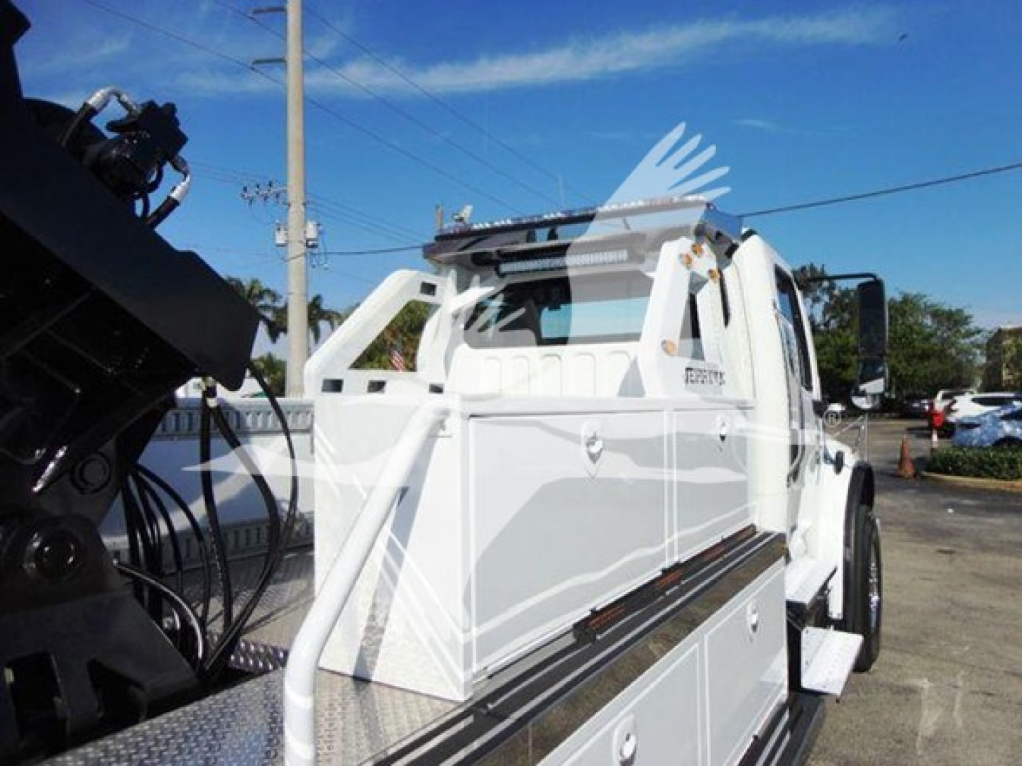 Freightliner Business Class M2 106 winch truck side view showing white body, hydraulic winch system, storage compartments, and cab; VIN label not visible.