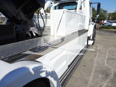 Tow truck with white body and black winch setup; long side step with diamond plate, cab in view.
