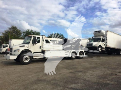 Freightliner Business Class M2 106 tow truck side view with winch, two white trucks parked on lot.