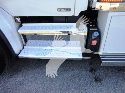 Step area of Freightliner Business Class M2 106 showing aluminum non-slip steps and a side panel with a red safety lever; partial badge area visible.