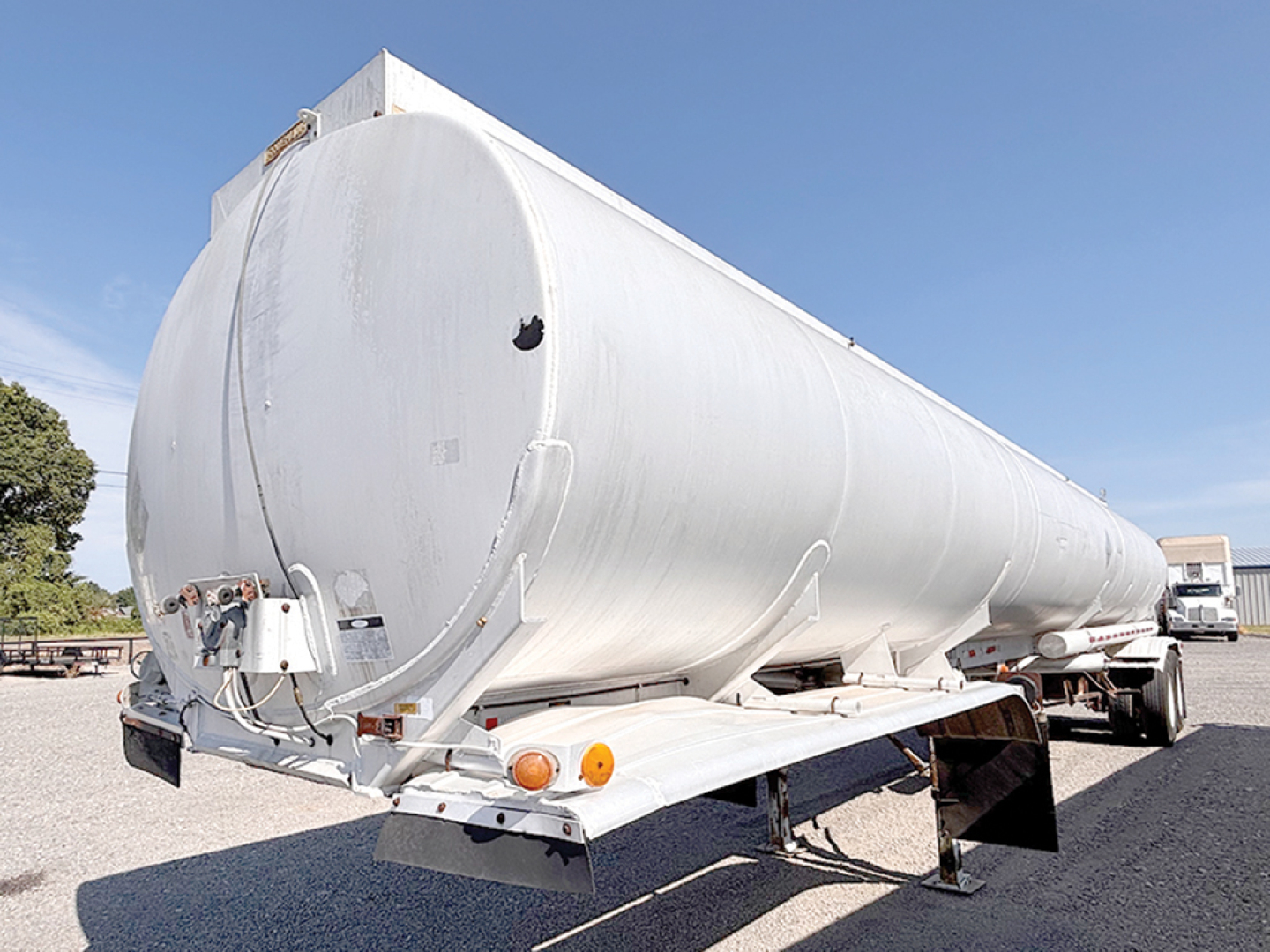 Aluminum petroleum tanker trailer in side view showing round tank, rear pump controls, and support legs.