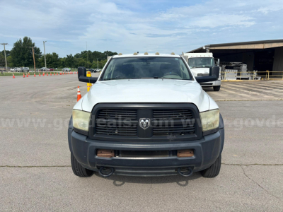 Front view of a white 2012 Dodge Ram 550 service/utility truck with black grille, bumper, and tow hooks; headlights, amber clearance lights on roof, and DMV-style lot in background.