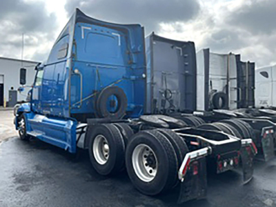 Semi truck tractor with blue sleeper cab and chrome wheels, rear view showing multiple wheel sets and trailing trailers; no legible serials or model text visible on the image