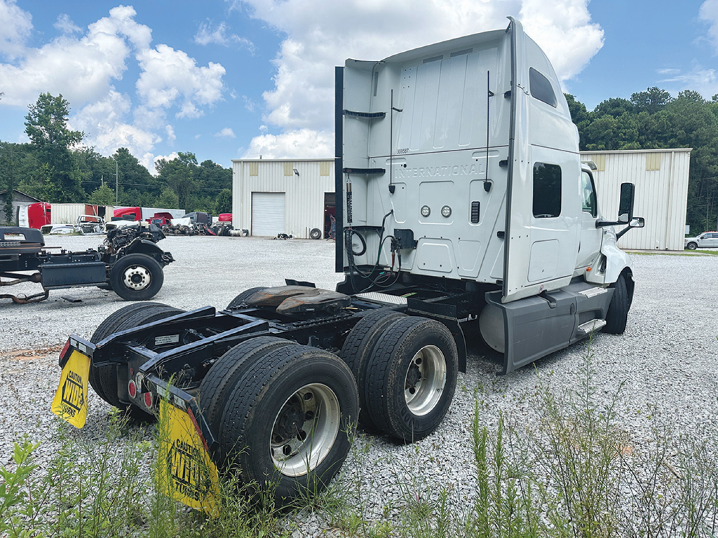Truck tractor rear view showing sleeper cab, fifth-wheel area, dual rear axles, and exhaust stacks; white paint; visible tires and chassis.