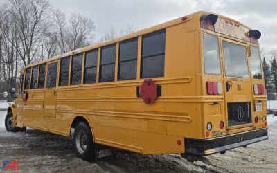 School bus rear-left view showing yellow Freightliner B2B bus with windows along side and back, rear lights, and bumper.
